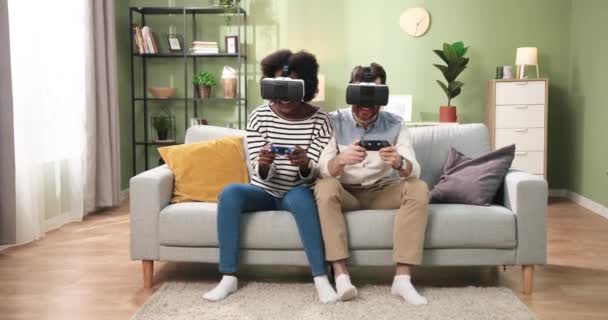 Χαρούμενες μικτές φυλές Αφροαμερικανή γυναίκα και Καυκάσιος άνδρας φορώντας γυαλιά εικονικής πραγματικότητας παίζοντας βιντεοπαιχνίδια χρησιμοποιώντας τεχνολογία εικονικής πραγματικότητας joysticks. Φίλοι που διασκεδάζουν μαζί στο σπίτι — Αρχείο Βίντεο