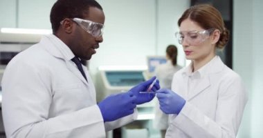 Afrika kökenli Amerikalı erkek ve beyaz önlüklü, gözlüklü beyaz önlüklü kadın laboratuvar çalışanları kan testi, örnek, aşı geliştirme çalışmaları yapıyorlar. Analiz kavramı