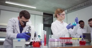 Modern tıp laboratuarında çalışan erkek ve kadın mikrobiyoloji uzmanları profesyonel mikroskop ekipmanları kullanarak deney yapıyorlar. Kadın laboratuvar uzmanı virüs tedavisini inceliyor.