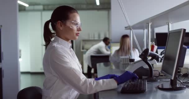 Beyaz önlük ve gözlüklerle dolu yoğun bir beyaz kafkas genç mikrobiyoloji uzmanı portresi. Laboratuvarda araştırma yapıyor. Test sonuçları üzerinde çalışıyor. — Stok video