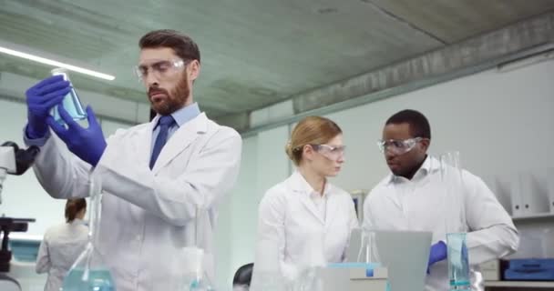 Portret van multi-etnische jonge team van mannelijke en vrouwelijke professionele laboratoriumspecialisten werkzaam in laboratorium in kliniek typen op laptop ontwikkelen vaccin holding tube met monster, genetisch onderzoek — Stockvideo