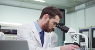 Klinik laboratuarında DNA mutasyonları üzerinde çalışan beyaz, yakışıklı, genç ve ciddi genetik bilimci portresi. Bilgisayardaki mikroskop ve daktilo sonuçlarıyla. Tıbbi araştırma konsepti