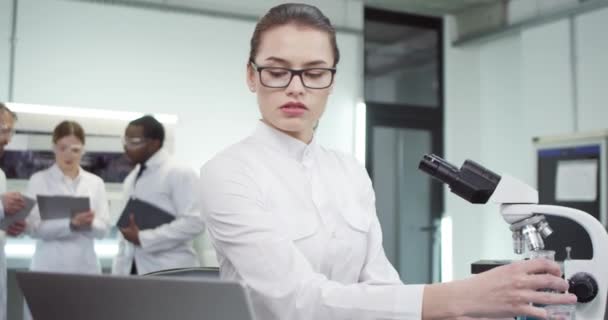 카프카스의 젊고 건강 한 여성 미생물학 과학자가 병원에서 백신 치료제를 개발하는 튜브에서 액체를 확인하고 노트북에서 결과를 타이핑하는 모습, 연구 개념 — 비디오