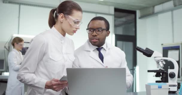 Portrait de jeunes scientifiques en microbiologie féminine et masculine de races mixtes discutant en laboratoire clinique des résultats d'expériences médicales, développant un vaccin, travaillant en laboratoire et naviguant sur tablette — Video