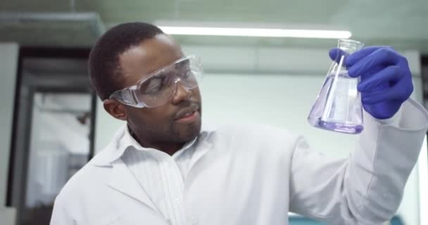Klinikte çalışan genç Afrikalı Amerikalı doktor bilim adamının portresi. İlaç aşısı geliştiriyorlar. Sıvı kimyasallarla deney yapıyorlar. — Stok video