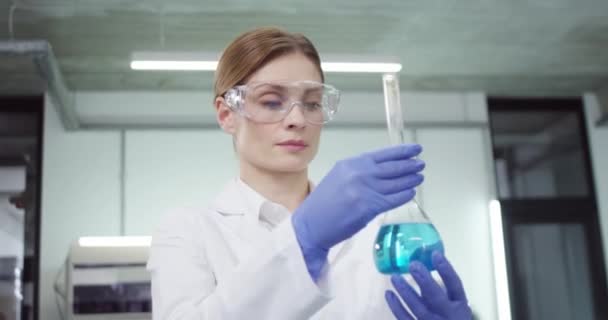 Close-up portret van blanke ernstige vrouwelijke gezondheidswerker medisch wetenschapper in bril in lab in ziekenhuis holding tube met blauwe vloeistof ontwikkelen van genezing uitvoeren van experiment, genetisch onderzoek — Stockvideo