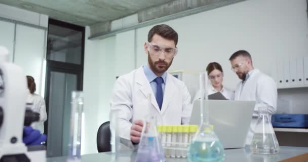 Врачебная команда смешанных рас из врачей ученых, работающих в лаборатории в клинике, кавказский человек, пишущий смс на ноутбуке, работающий над вакциной — стоковое видео