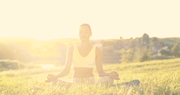 Blanke vrouwelijke yogi zittend op gras met gesloten ogen en mediterend in lotushouding. Yoga asana voor meditatie. Vroege ochtend. Portret van een mooie gelukkige vrouw die ogen opent en glimlacht naar de camera. — Stockvideo