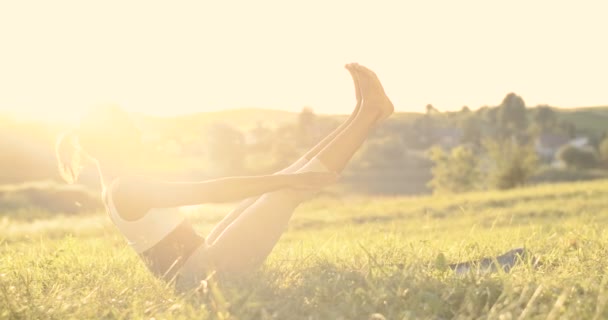 Jolie jeune femme sportive yogi assis sur l'herbe verte et l'équilibre avec les mains levées et les jambes vers le haut. En plein soleil. Femme commençant la journée d'été avec l'exercice et le yoga. Belle nature. Étirement asana. — Video