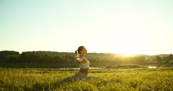 Beyaz, genç, dişi yogi yeşil çimlerin üzerinde uzanıyor, sonra meditasyon yapmak ve nefes almak için ellerini kaldırıyor. Güzel kırsal doğa. Yogadaki sporcu kadın yaz sabahından itibaren esneme hareketleri yapıyor.. — Stok video