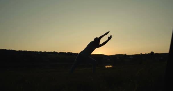 Man mörk siluett av yogi stående i naturen och gör yoga. Man böjer sig med händerna i asana utomhus. Solnedgång eller ner på sommaren. — Stockvideo