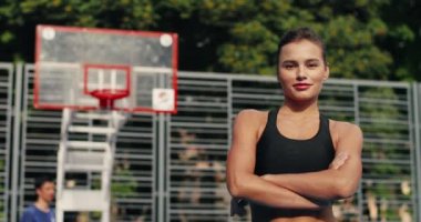 Güneşli bir günde basketbol sahasında dikilirken kameraya gülümseyen neşeli, genç ve güzel bir bayan. Yüzünde gülümseme olan mutlu beyaz bir kızın portresi. Spor yaşam tarzı konsepti