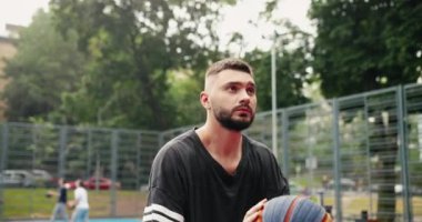 Beyaz tenli konsantre erkek sokak basketbolcusunun kapanışı yerel sahada basketbol oynarken saha golü atmaya çalışıyor. Sporcu hünerleri. Portre konsepti