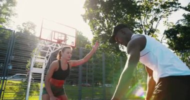 Açık havada sokak basketbolu oynayan melez gençlerin portresi. Güzel beyaz kız ve Afrikalı Amerikalı erkek basketbolcular yerel kortta oynuyor. Top potaya çarptı. Rekabet konsepti