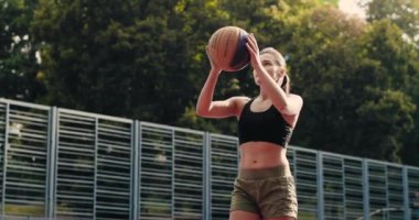 Güzel, genç, mutlu, beyaz kadın basketbolcunun portresi. Açık şehir çocuk parkında antrenman yapıyor ve topu potaya atıyor. Sahadaki güzel sporcu kadın. Sokak topu konsepti