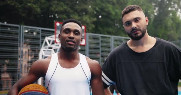 Zbliżenie wieloetnicznych koszykarzy męskich wycieranie potu rękami po ciężkim treningu. Afroamerykańscy i kaukascy sportowcy stoją na boisku po meczu. Streetball w mieście Koncepcja portretu — Wideo stockowe