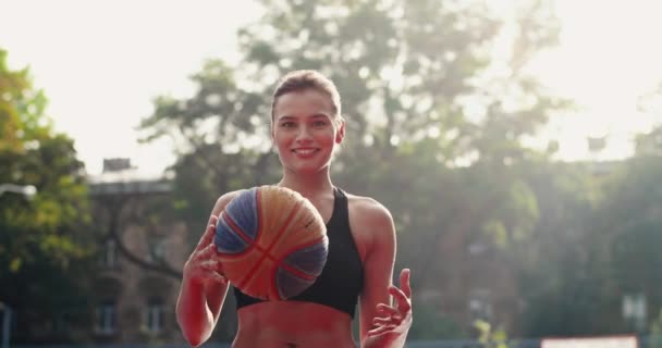 Zamknij portret radosnej młodej kobiety profesjonalny koszykarz rzucając piłkę między rękami na zewnątrz boiska. Piękna biała dziewczyna ćwiczy streetball i rzuca piłkę. Koncepcja sportu — Wideo stockowe