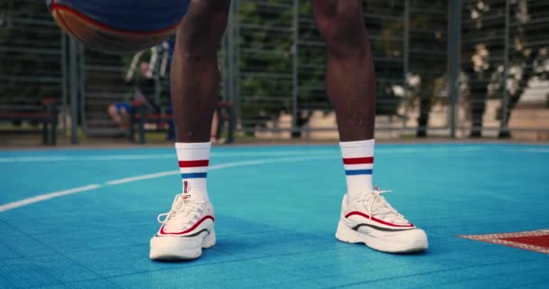 Giocatore di basket maschile attivo che pratica l'abilità di maneggio della palla, dribbling palla tra le gambe sul campo all'aperto. Primo piano di afroamericani gambe uomo in calzini bianchi di formazione cross bouncing con palla — Video Stock