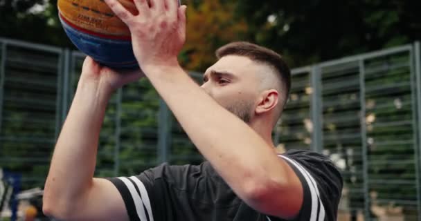 Портрет красивого молодого кавказского профессионального баскетболиста, практикующего мастерство на открытой площадке и бросающего мяч. Крупный план тренировок на местном суде в городе. Концепция — стоковое видео