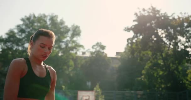 Close up portrait of beautiful young serious Caucasian basketball female player practicing skills on outdoor court and throwing ball. Girl playing streetball on urban playground. Training concept — Stock Video