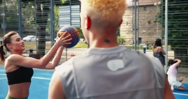 Nahaufnahme Portrait von gemischten Rassen junge Männer und Frauen spielen Streetball im Freien. Schöne kaukasische Mädchen und afroamerikanische männliche Basketballspieler, die auf einem lokalen Platz spielen. Mädchen werfen Ball. — Stockvideo