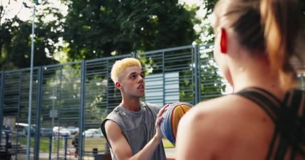 Närbild porträtt av blandraser unga manliga och kvinnliga idrottare spela streetball utomhus. Vacker vit flicka och afroamerikansk pojke basketspelare spelar på urban domstol Guy kasta boll. — Stockvideo