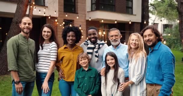 Ritratto di famiglia felice di razze miste a cena all'aperto in cortile sorridente e in posa davanti alla telecamera durante il fine settimana trascorrendo insieme. Persone multietniche al barbecue. Festeggiamenti. Genitori e figli. Generazioni. — Video Stock