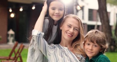 Orta yaşlı beyaz kadın portresi. Küçük, kızıl saçlı bir oğlu ve kameraya gülümseyen güzel bir kızı var. Açık havada. Güzel anne, küçük oğlan ve kız. Mutlu annelik.