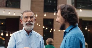 Yakışıklı beyaz, yaşlı ve genç iki adam, evin arka bahçesinde dikilip konuşuyorlar. Aile yemeği arka planda. Yetişkin oğlu olan büyük baba konuşuyor. Nesiller.