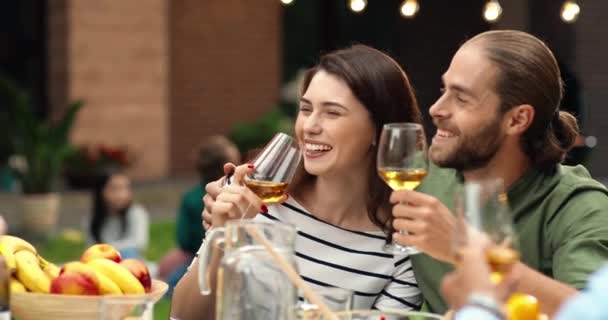 Glada vita glada par med drinkar sitter i kramar och skrattar åt familjemiddag grill utomhus. Glädjande romantisk man och kvinna förälskade vid bordet. Besök och möte med föräldrar. — Stockvideo
