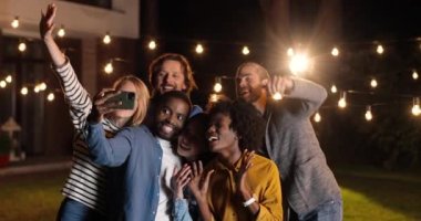 Karışık ırklar genç mutlu ve neşeli arkadaşlar, erkekler ve kadınlar gece selfie çekerken akıllı telefona gülümseyip poz veriyorlar. Gece yarısı partisi. Çoklu etnik erkek ve kadınlar eğleniyor.
