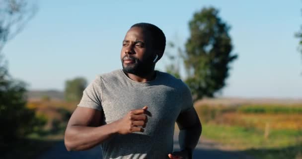 Afro-Amerikaanse knappe sterke mannelijke jogger in koptelefoon loopt op de weg op het platteland op de zomerdag. Aantrekkelijke sportieve man aan het joggen buiten. Sport concept. Sportman hardloper. Ochtendnatuur. — Stockvideo