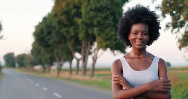 Porträt einer hübschen afroamerikanischen Joggerin mit lockigem Haar, die an einem Sommertag auf der Straße steht und lächelt. Sportliche Frauen lächeln draußen. Sportkonzept. Sportlerin. — Stockvideo