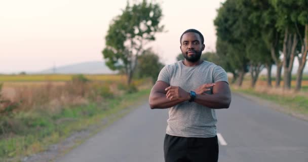 Retrato de afro-americano bonito corredor masculino com relógio inteligente em pé na estrada no campo no dia de verão, cruzando as mãos e sorrindo. Homem desportivo a correr ao ar livre. Desporto. Esportista corredor. — Vídeo de Stock