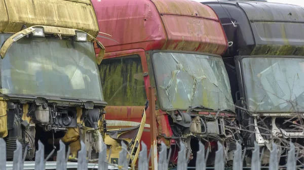Farklı renklerde hurda nakliye araçları bir arada depolanmış. Tüm kamyonlar sorunlu, yıpranmış ve parçalanmış durumdalar. Metal korkulukların arkasında açık havada duruyor. İngiltere.