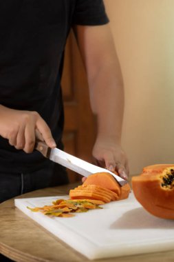 Tahta bir masanın üzerinde taze papaya kesen bir adam. Sağlıklı beslenme kavramı.