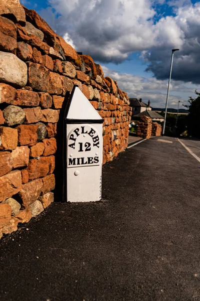 A A mile marker on a road outside a new housing estate on the outskirts of Penrith Cumbria United Kingdom showing 12 miles to Appleby