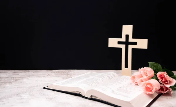 church composition with wooden cross , bible and Beautiful pink flowers on white background, space for text.