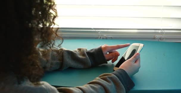 Kıvırcık Saçlı Kadın Cep Telefonu Uygulamasını Kullanarak Kaydırıyor Pencerenin Yanında — Stok video