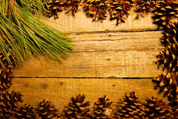 Rectangular frame of pine cones and a green pine branch on an old table with a great wooden texture. Ideal for Christmas or autumn.