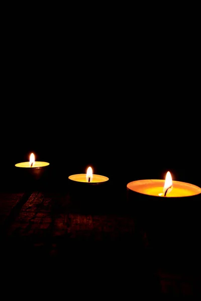 Drei Brennende Teewachskerzen Auf Einem Holztisch Vor Schwarzem Hintergrund — Stockfoto