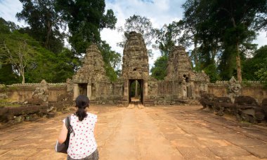 Angkor Bat 'ta beyaz tişört ve çanta giymiş genç bir kadın tapınağa doğru yürüyor.