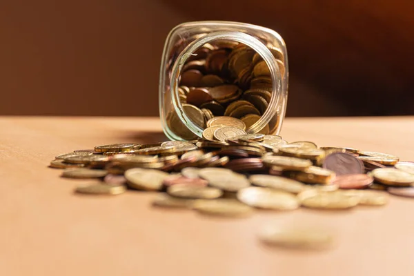 Half empty money jar with coins over the table. Front view. Save money concept banner