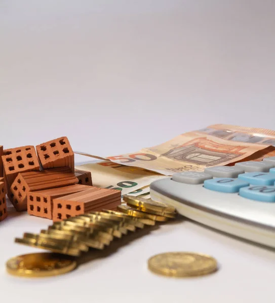 Pile of bricks, coins and euro notes next to a calculator on a white background. Home loan real estate for mortgage concept.