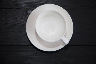 Beyaz porselen bardak boş, tabağı koyu ahşap arka planda..