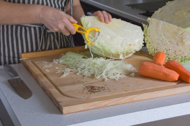 Üç parlak havuç ve büyük sulu lahana kafası, parçalara ayrılmış, kesme tahtasına uzanmış, bir kadın sebze soyacağı ile lahana kesiyor..