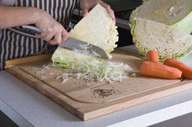 Üç parlak havuç ve kesme tahtasının üzerinde büyük, sulu bir lahana kafası, bir kadın büyük bir mutfak bıçağıyla lahana kesiyor.