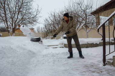 Adam evinin bahçesinden plastik bir kürekle kar fırlatıyor.