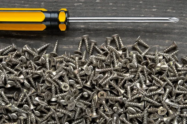Screwdriver with a yellow handle and a lot of screws — Stock Photo, Image