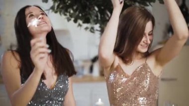 Parlak elbiseli iki kadın maytaplarla dans ediyor ve Noel 'de gülümsüyor.